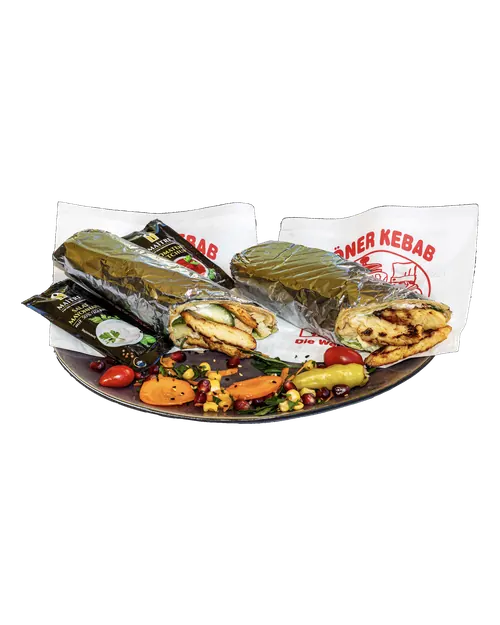 Zwei Chicken Wraps in Folie, daneben Gemüse und Dips
